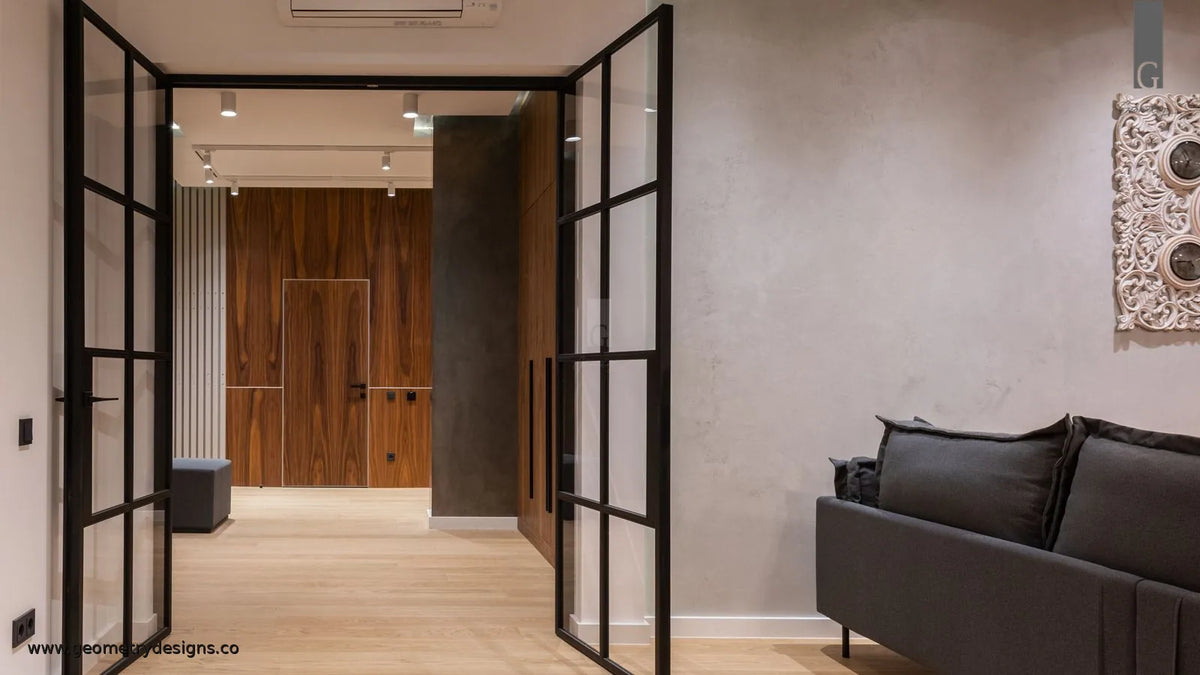 Luxury foyer entryway with open Crittall-style glass doors, warm wood-paneled wall beyond, and a calm transition into the living space