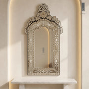 Geometry Designs Venetian Mirror in etched silver glass with studded frame and crest, shown above a white marble console in a warm arched niche.